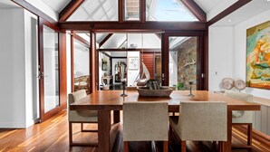 A dining area with a wooden table and chairs, a large window, and a view of the interior. - Luxury On The Bay 2 - Ocean Views (Byron Bay)