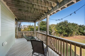 A covered outdoor deck with a wooden railing, a hammock, and a chair.