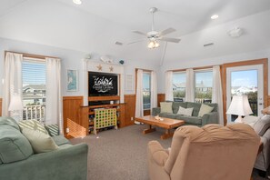 A spacious living room with a television, a ceiling fan, and a view of the city.