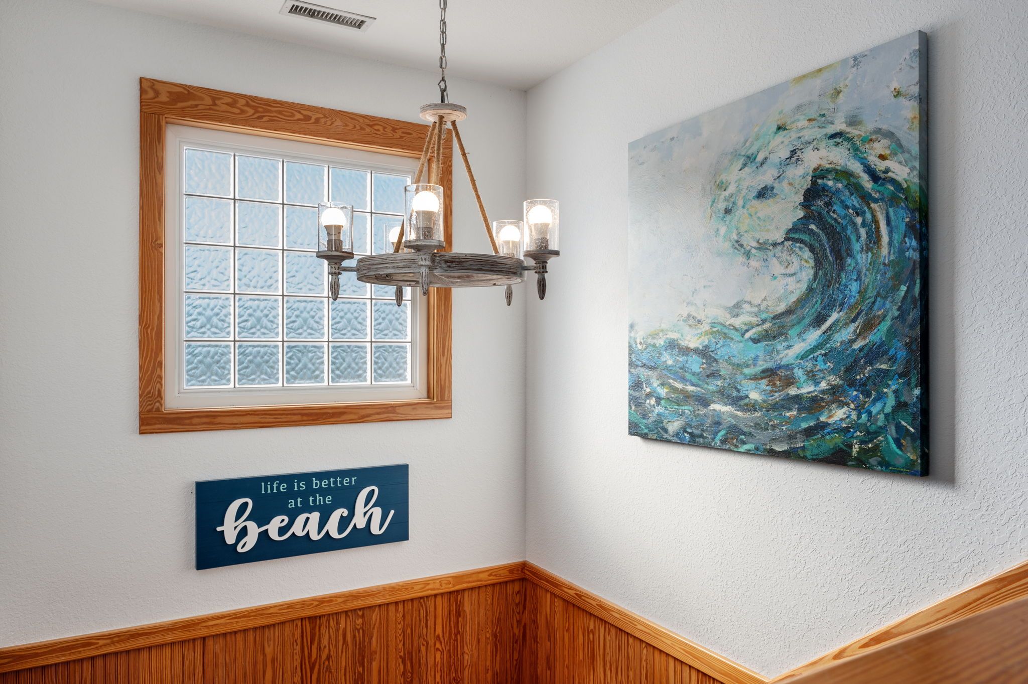 Une pièce avec un mur lambrissé en bois, un lustre, une fenêtre donnant sur un beau paysage et un tableau représentant une vague.