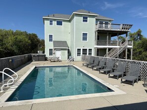 A two-story building with a pool, outdoor seating, and a staircase leading to a balcony. - Beachnuts Too: Pet Friendly, Oceanside, Private Pool and Hot Tub (Corolla)