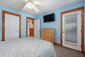 A bedroom with a bed, a dresser, a ceiling fan, a TV, and a door with blinds.