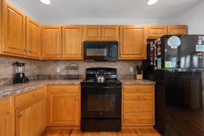 A kitchen with wooden cabinets, a black stove, a microwave, and a refrigerator.