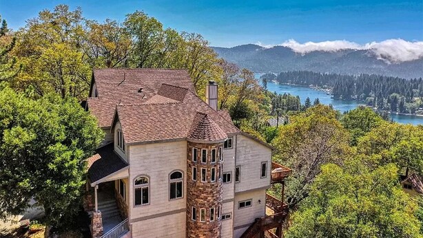 A large, multi-story house with a turret, surrounded by lush greenery and overlooking a lake. - Charming 4-bedroom chalet with AC and WiFi in gorgeous Lake Arrowhead (Lake Arrowhead)