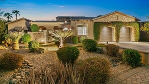 A two-story house with a stone facade, a covered patio, and a landscaped garden with various plants and a rock bed. - Rare Gem: Pool, Spa, Game Room, Fire Table! (Indio)