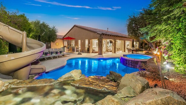 A swimming pool with a slide, outdoor seating, and a building with a tiled roof. - Rare Gem: Pool, Spa, Game Room, Fire Table! (Indio)