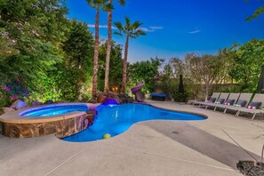 A swimming pool with a hot tub, surrounded by palm trees and lounge chairs.