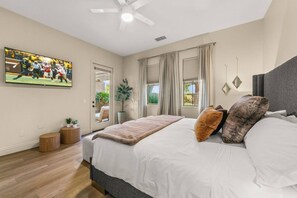 A bedroom with a bed, a ceiling fan, a TV on the wall, and a window with curtains.