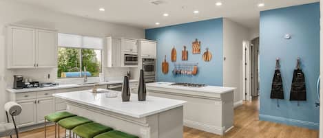 A modern kitchen with white cabinetry, a central island with stools, and a blue accent wall with hanging kitchen tools.