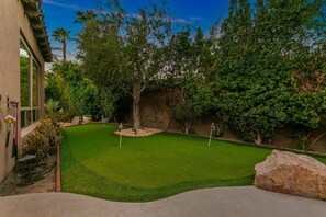Ein gepflegter Garten mit Putting-Green, einem großen Baum und einer Steinmauer.