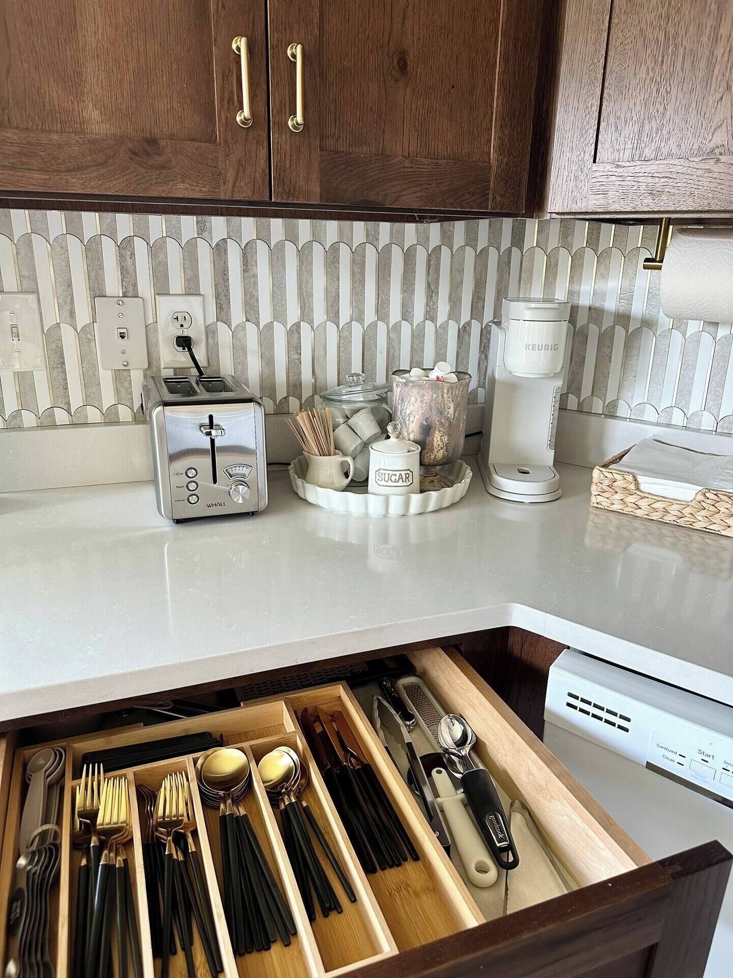 Cucina con mobili in legno, un tostapane, una macchina da caffè e un organizer cassetti con utensili.