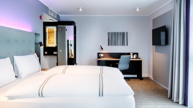 A hotel room with a large bed, a desk, a chair, a TV, and a wardrobe. - Premier Inn Lübeck City Centre (Lubeck)