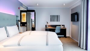 Habitación de hotel con una cama grande, un escritorio, una silla, un televisor y un armario.