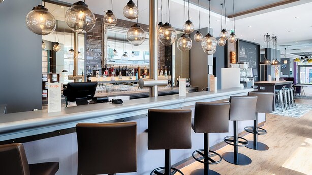 Un área de bar moderna con lámparas esféricas colgantes, una barra con menú y taburetes.