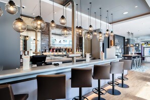 A modern bar area with hanging spherical light fixtures, a counter with a menu, and bar stools. - Premier Inn Lübeck City Centre (Lubeck)