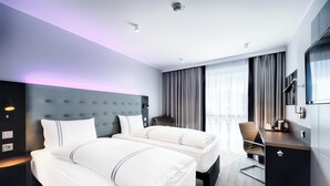 A hotel room with two beds, a desk, a chair, a TV, and a large window with curtains. - Premier Inn Lübeck City Centre (Lubeck)