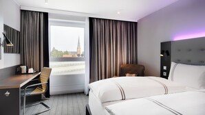 A hotel room with a bed, a desk, a chair, and a view of a building outside. - Premier Inn Lübeck City Centre (Lubeck)