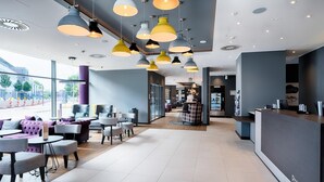 Un moderno vestíbulo de hotel con mostrador de recepción, zona de estar con sofás y mesas, e iluminación colgante.
