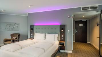 A hotel room with a large bed, a chair, a nightstand, a wall-mounted clock, and a door leading to another room.