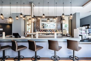 Zona de bar con varios taburetes, lámparas colgantes y una barra con diferentes botellas.