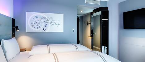 A hotel room with a bed, a wall clock, a television, and a door leading to a bathroom.