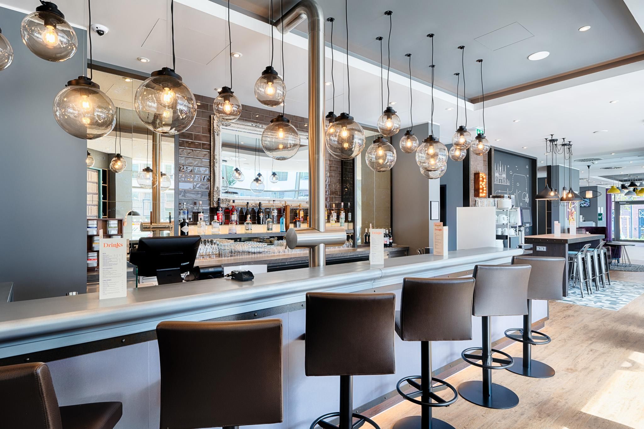 Un área de bar moderna con lámparas esféricas colgantes, una barra con menú y taburetes.