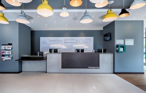 Zona de recepción de un hotel con diseño moderno, que incluye un mostrador de recepción, una gran pared con citas motivacionales y varias lámparas colgantes.