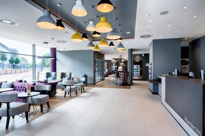 A modern hotel lobby with a reception desk, seating area with couches and tables, and pendant lighting.