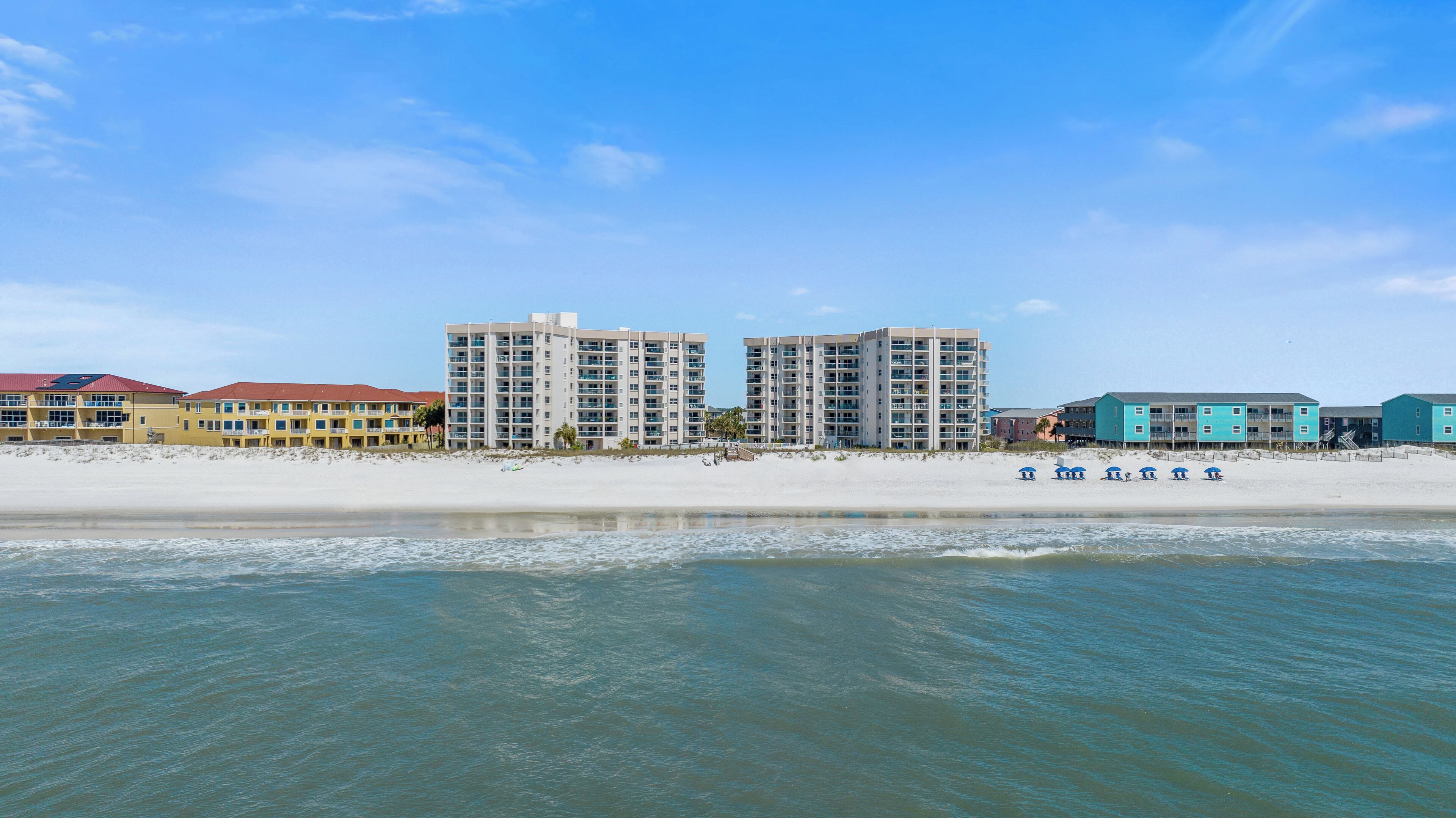Ein Strandhotel mit mehreren Hochhäusern, einem Sandstrand und einem klaren, blauen Himmel.