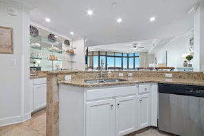 A kitchen with white cabinetry, granite countertops, a dishwasher, and a large window offering a view.