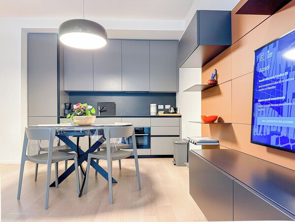 A modern kitchen with grey cabinets, a dining table with chairs, and a TV mounted on the wall displaying an advertisement.