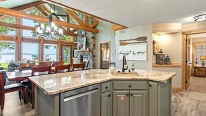 A kitchen with a large island, wooden beams, stone accents, and a view of the outdoors. - Lakefront Townhome | 6BR | Man Cave + Lake View (Nisswa)