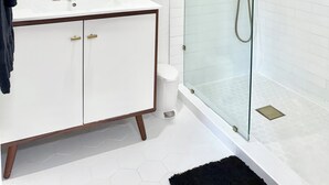 A modern bathroom with a glass-enclosed shower, a white vanity with gold fixtures, and a round mirror.