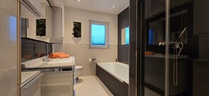 Ett modernt badrum med en vit tvättställ, ett badkar och en duschkabin med glasväggar.