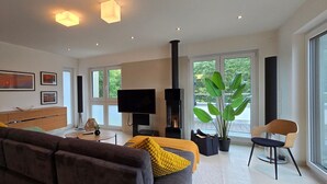 A modern living room with a sofa, coffee table, TV, fireplace, and large windows.