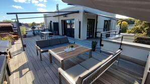 A modern outdoor deck with a wooden floor, a sofa, a table, and a railing.