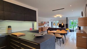 A modern kitchen with dark cabinetry, a central island, and a dining area with a round table and chairs.