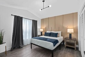 Una moderna camera d'albergo con un letto grande, due comodini con lampade, un lampadario e un'ampia finestra con tende.