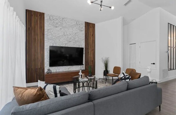 Un soggiorno moderno con un'ampia televisione a schermo piatto, un divano grigio, un tavolino da caffè e una parete decorativa in legno.