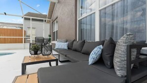 Een overdekt terras met een zwembad, een bank met kussens en een tafel met stoelen.