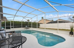 Una piscina all'aperto con una veranda coperta, circondata da un recinto bianco e un siepe.