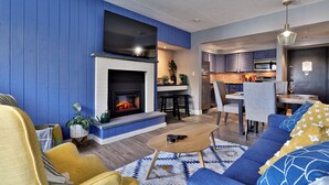 A modern living room with a fireplace, a dining area, and a kitchen.