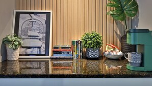 A kitchen counter with a framed picture, a coffee maker, a potted plant, a bowl of eggs, and a stack of books.