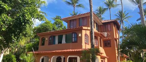 A two-story building with a red-tiled roof, surrounded by palm trees and lush greenery.
