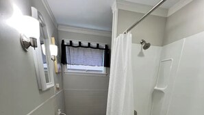 A bathroom with a pedestal sink, a bathtub, a window with blinds, and a green bath mat. - Cozy Downstairs Apartment (Uniontown)