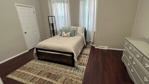 A bedroom with a bed, a dresser, a window with curtains, and a door. - Cozy Downstairs Apartment (Uniontown)