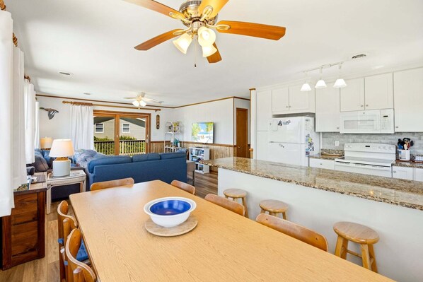 Una cocina moderna con armarios blancos, encimera de granito y comedor con mesa y sillas de madera.