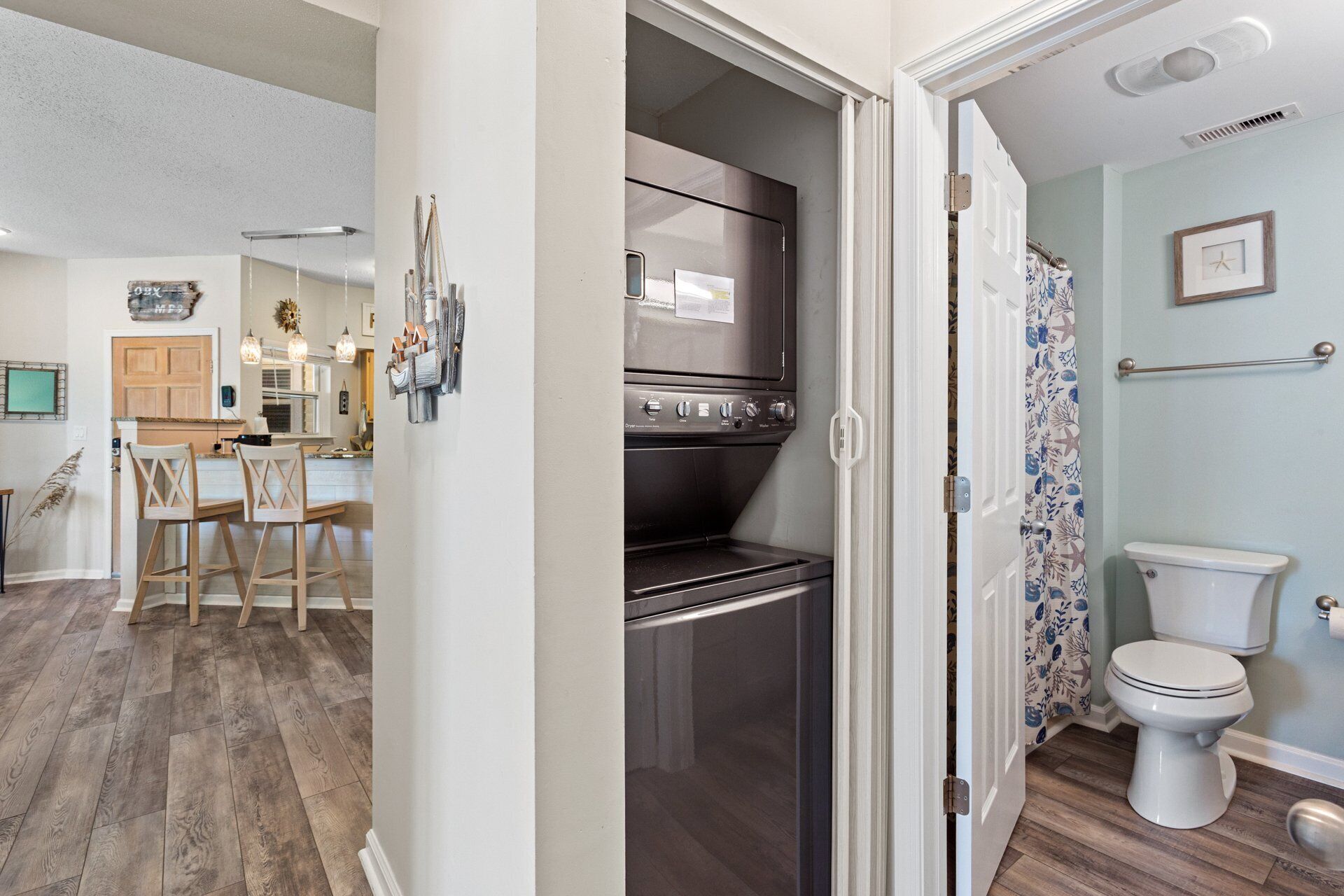 A compact kitchen with a built-in oven and microwave, a dining area with wooden chairs, and a bathroom with a toilet and shower curtain.