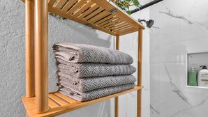 A bathroom with a wooden towel rack holding folded towels, a marble wall, and a shelf with toiletries.