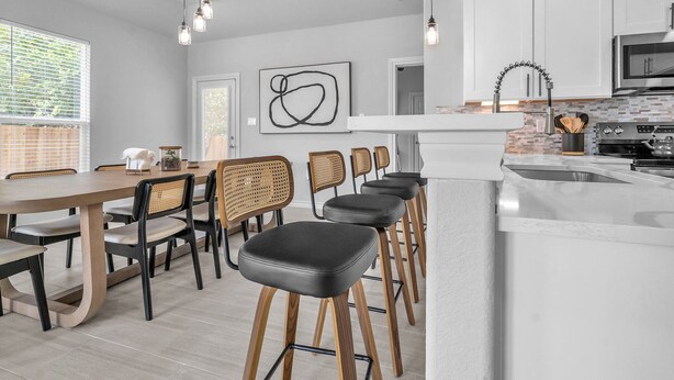 A modern kitchen with white cabinets, a stainless steel oven, and a bar area with stools.